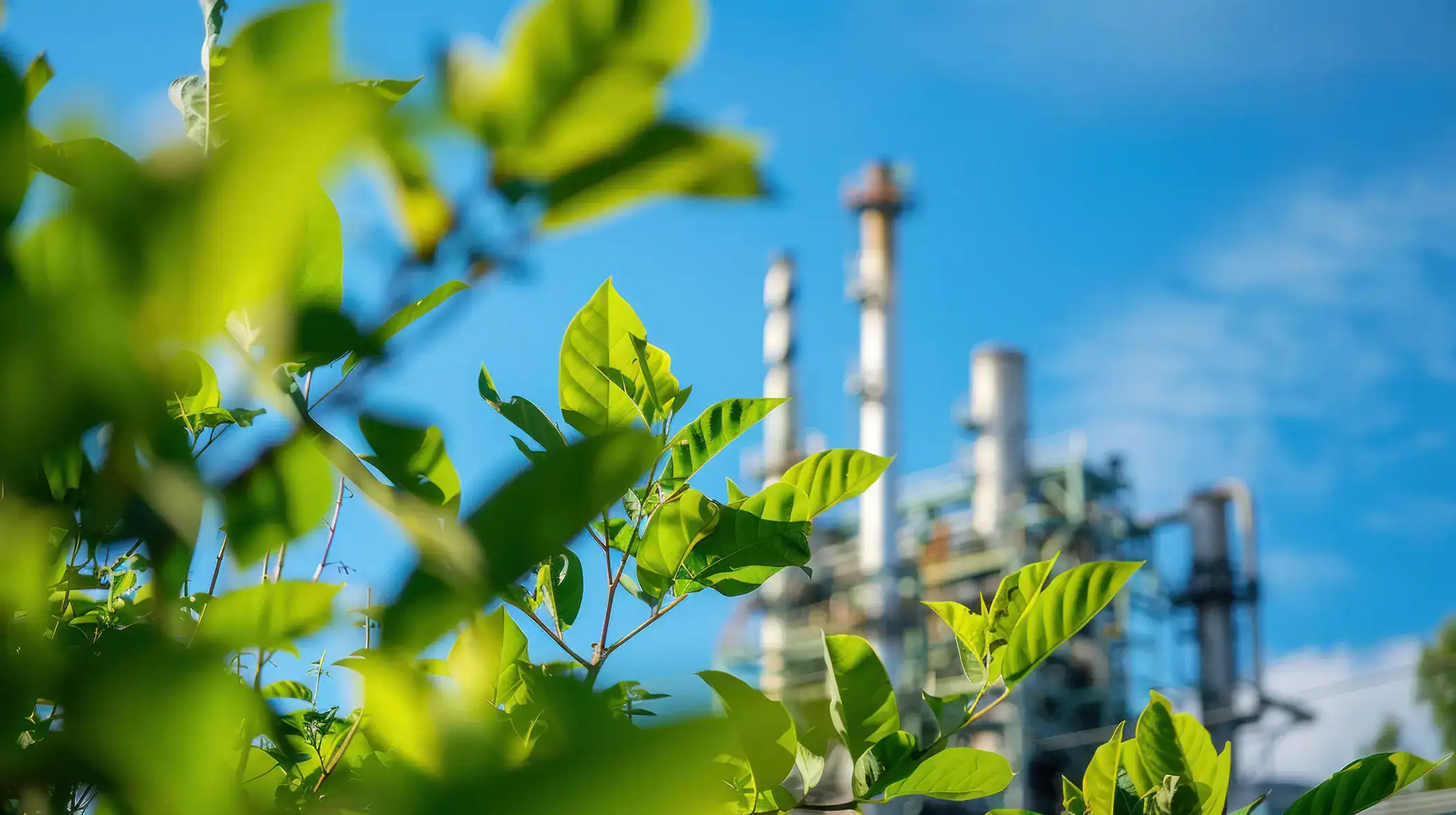 Green leaves with industrial plant in background, eco-friendly energy.